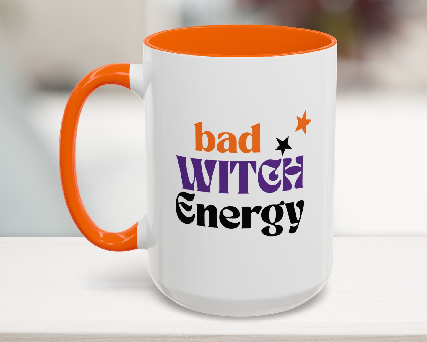 White mug with orange handle and 'bad witch energy' text on a blurred background