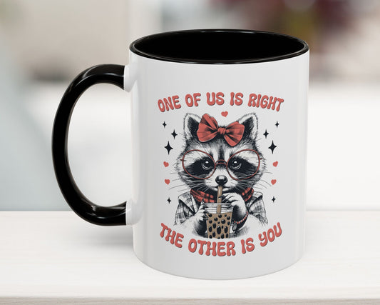 Mug with a raccoon design and text 'One of us is right, the other is you' on a blurred background