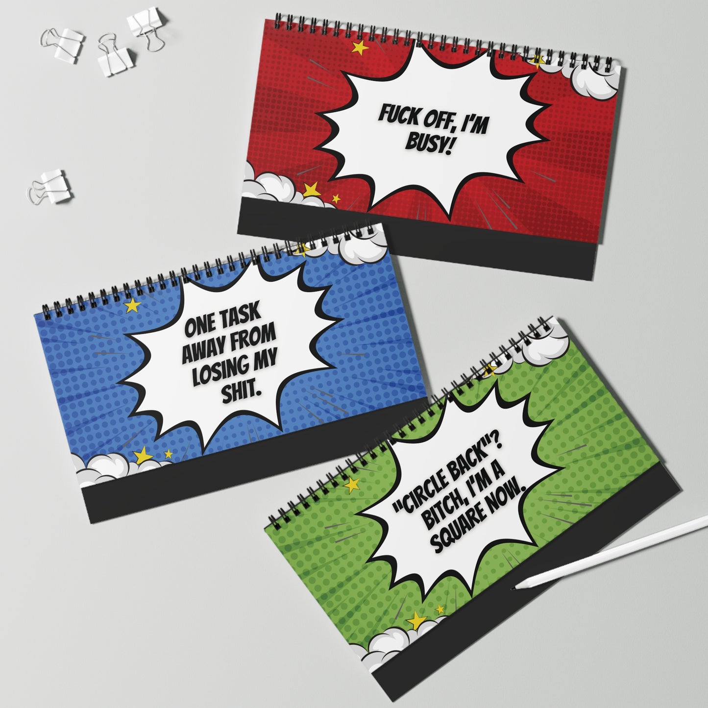 Three spiral-bound desk sign pages with colorful comic-style text on a gray background