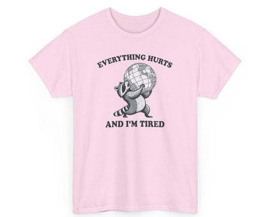 Light pink unisex tee featuring a tired raccoon with the phrase 'Everything Hurts and I’m Tired,' perfect for those who relate to the struggle.