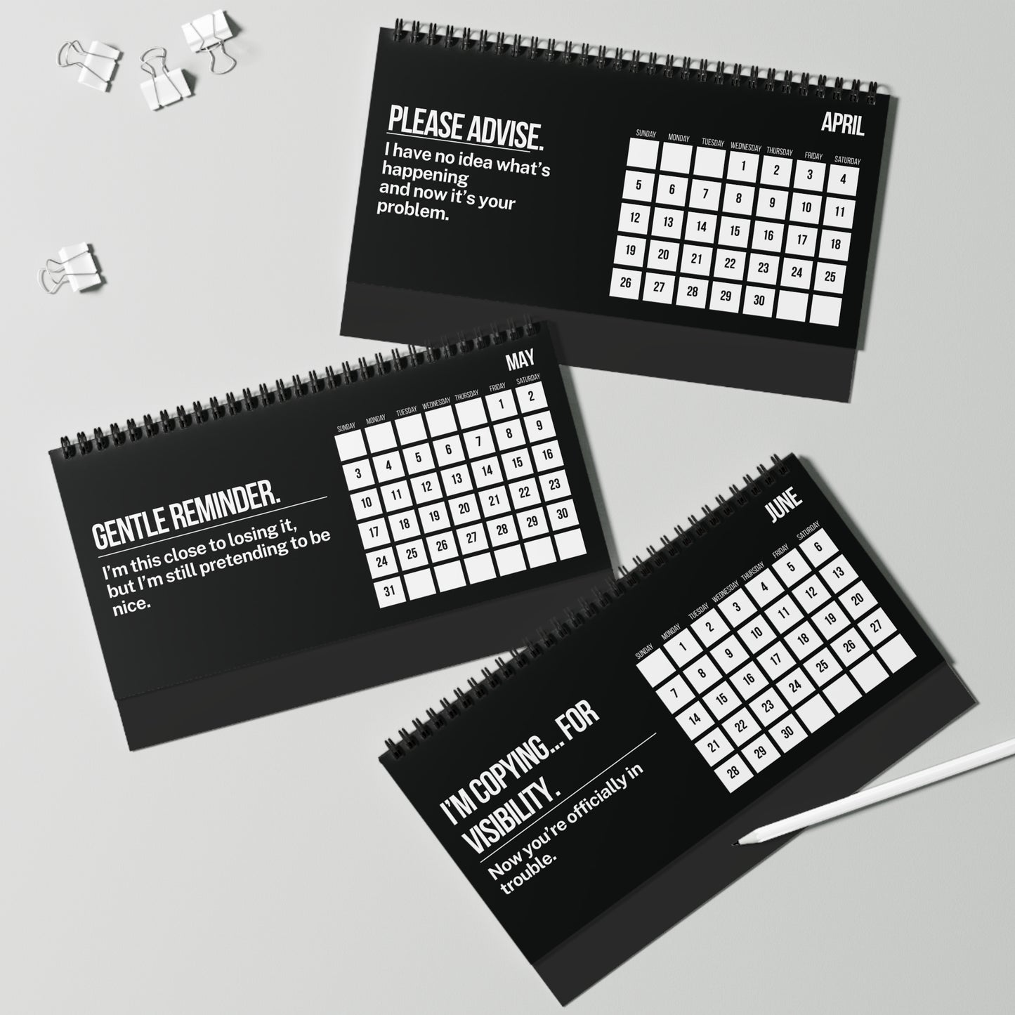 Three black spiral-bound calendars with humorous text for April, May, and June on a light gray background.