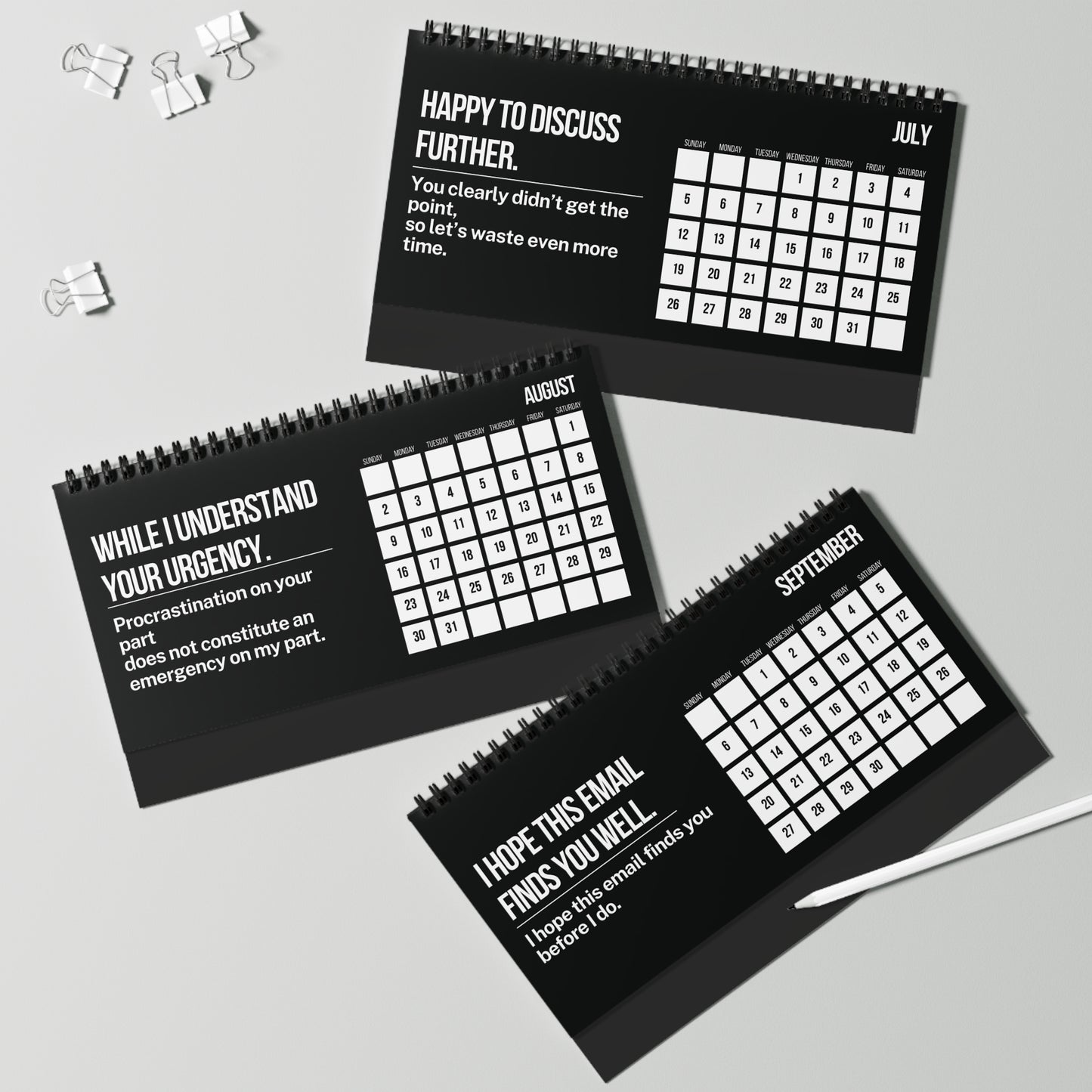 Three black spiral-bound calendars with white text on a gray surface.