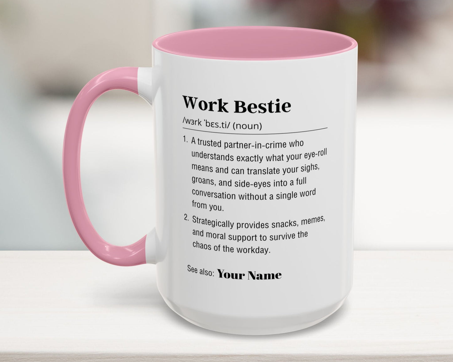 Mug with pink interior and handle featuring a definition of 'Work Bestie' on a blurred background