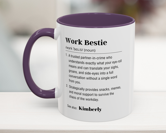 Mug with purple interior and handle displaying a definition of 'Work Bestie' on a blurred background