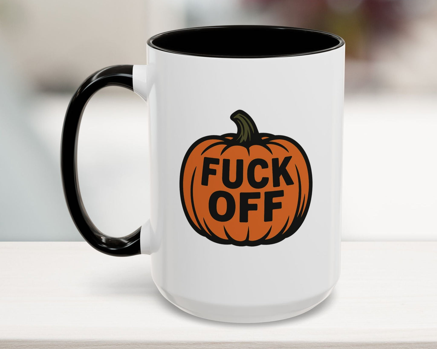 White mug with black interior and handle, featuring an orange pumpkin with text on a blurred background.