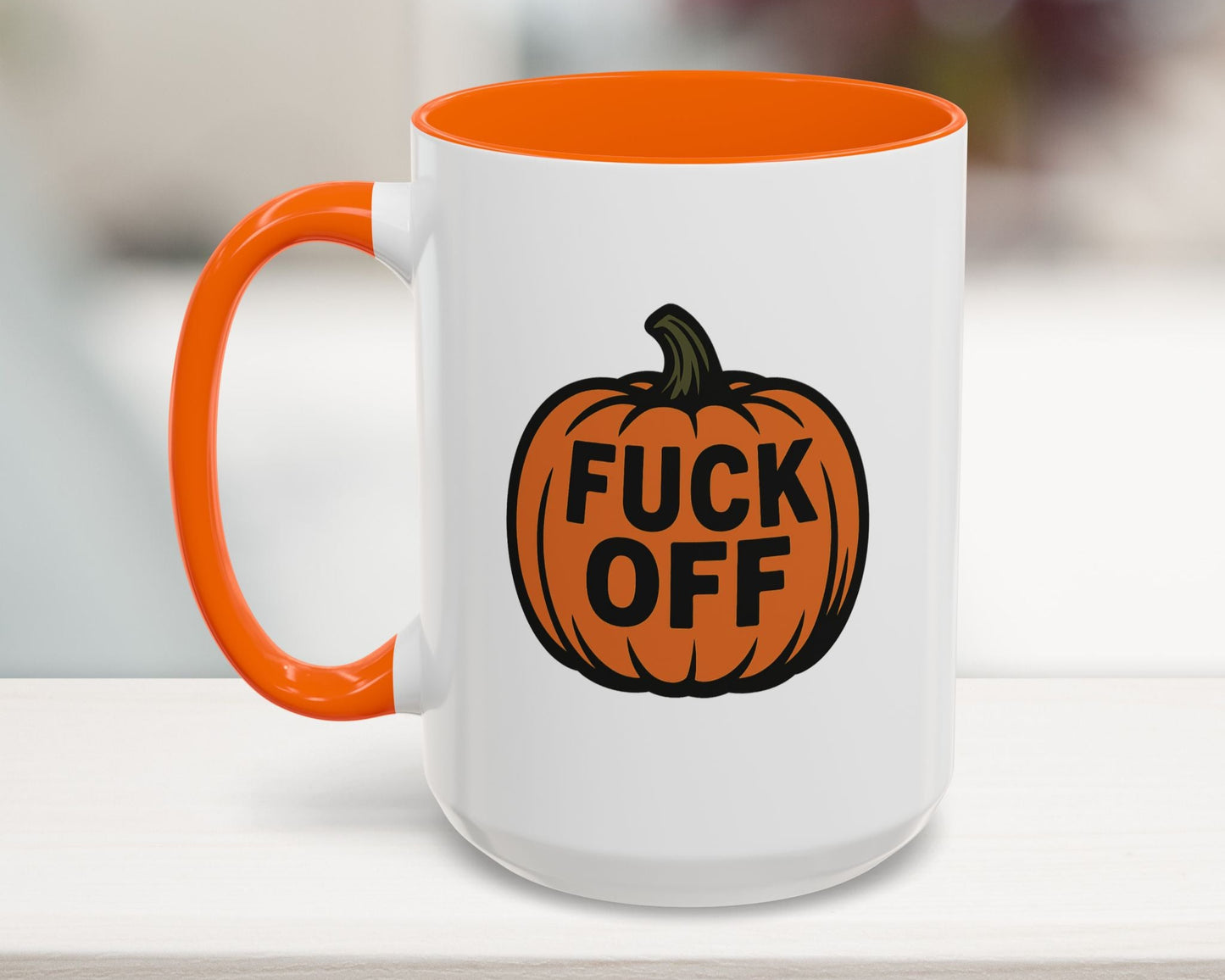 White mug with orange interior and handle, featuring a pumpkin design with text on a blurred background.