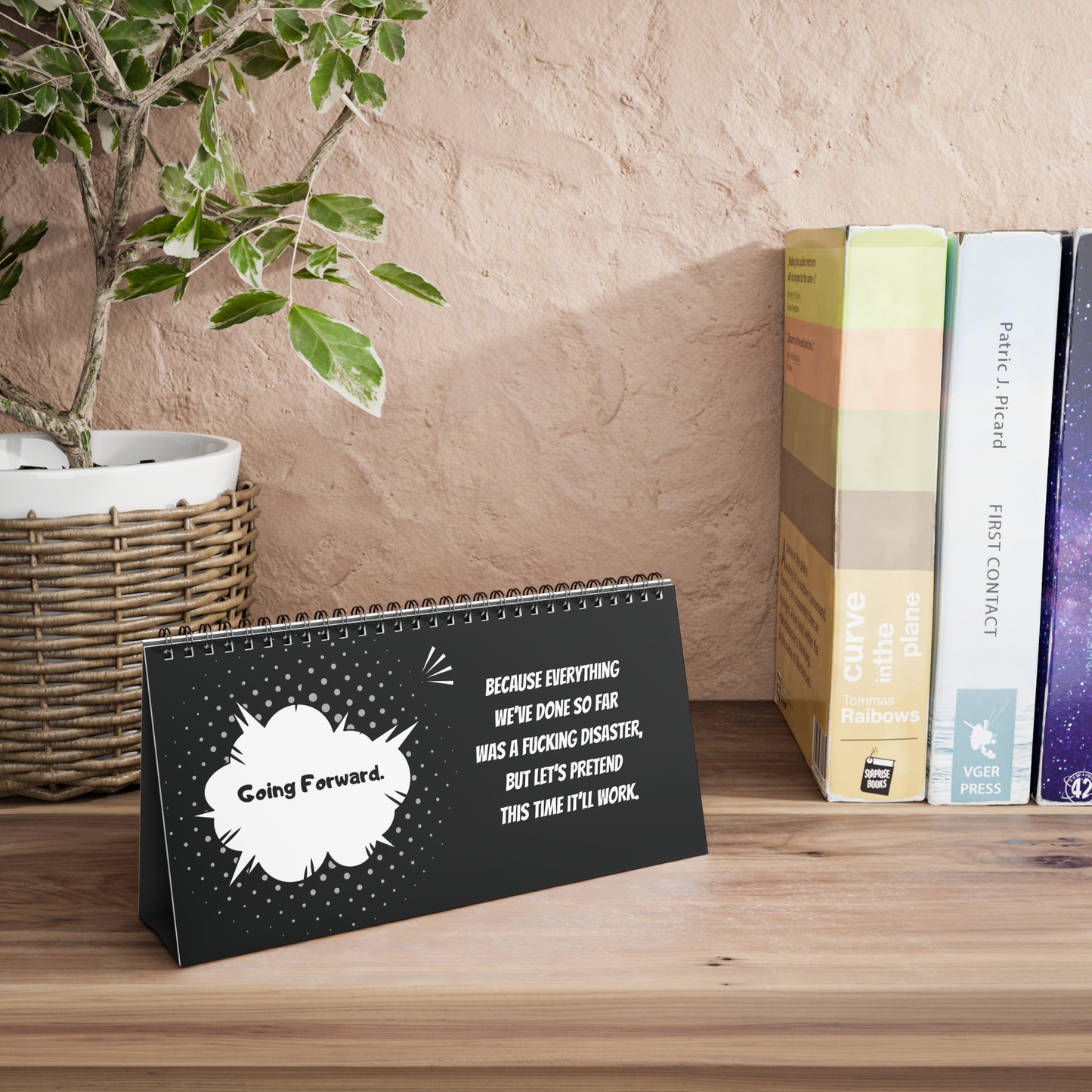 Desk calendar with motivational quote on a wooden surface with books and a plant in the background