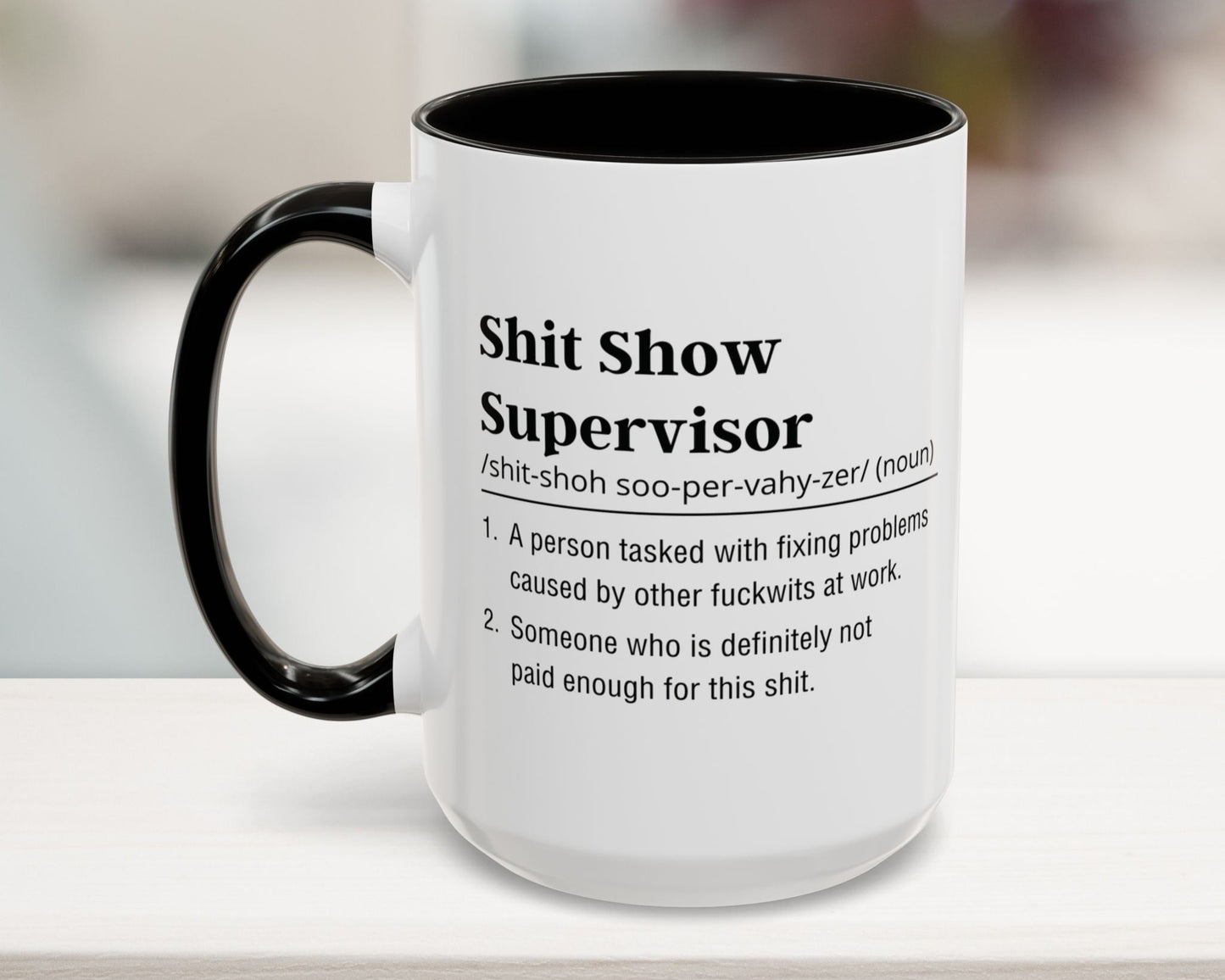 Mug with text definition of 'Shit Show Supervisor' on a blurred background