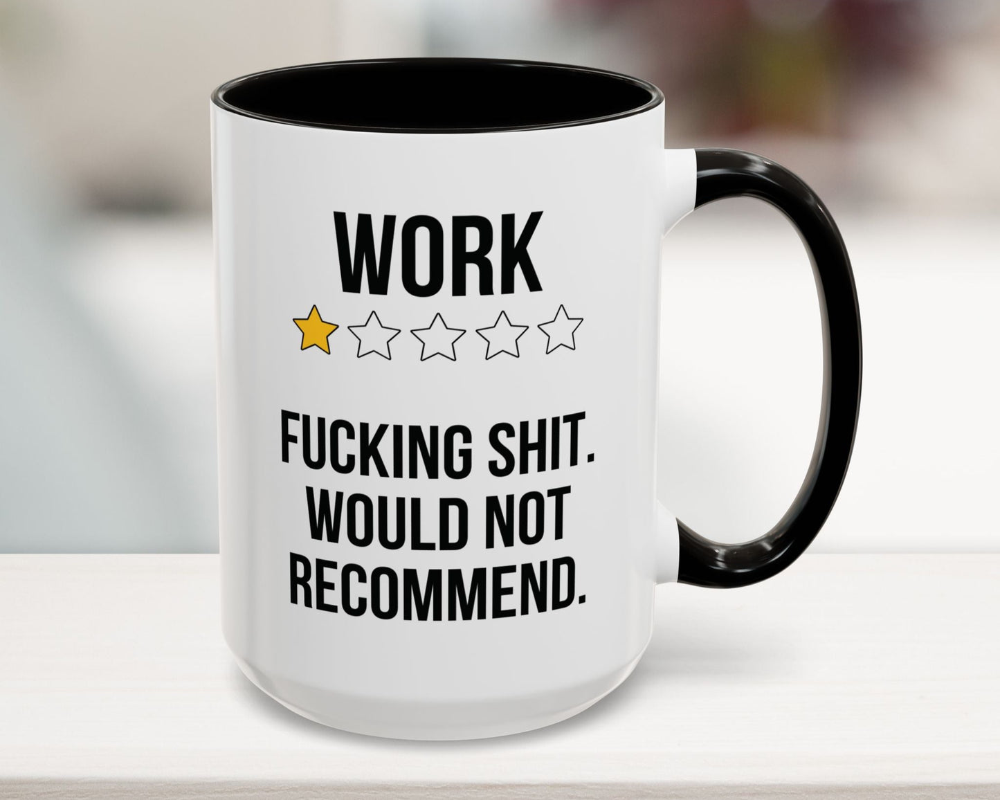 Mug with text 'WORK ★★★★ F***ING SHIT. WOULD NOT RECOMMEND.' on a blurred background