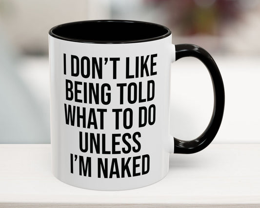 White mug with black interior and handle, featuring a humorous quote on a blurred background.