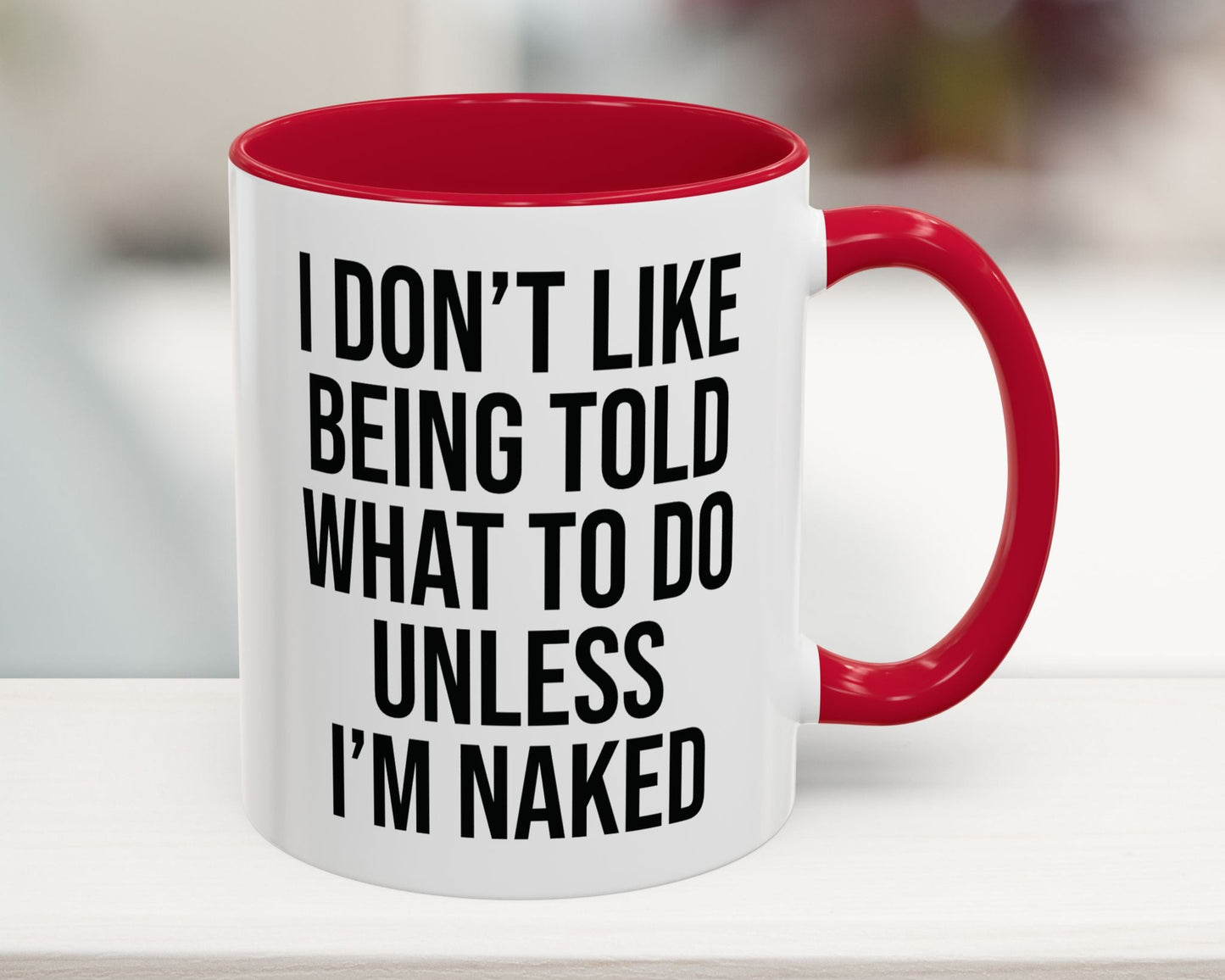 White mug with red interior and handle featuring a humorous quote on a blurred background