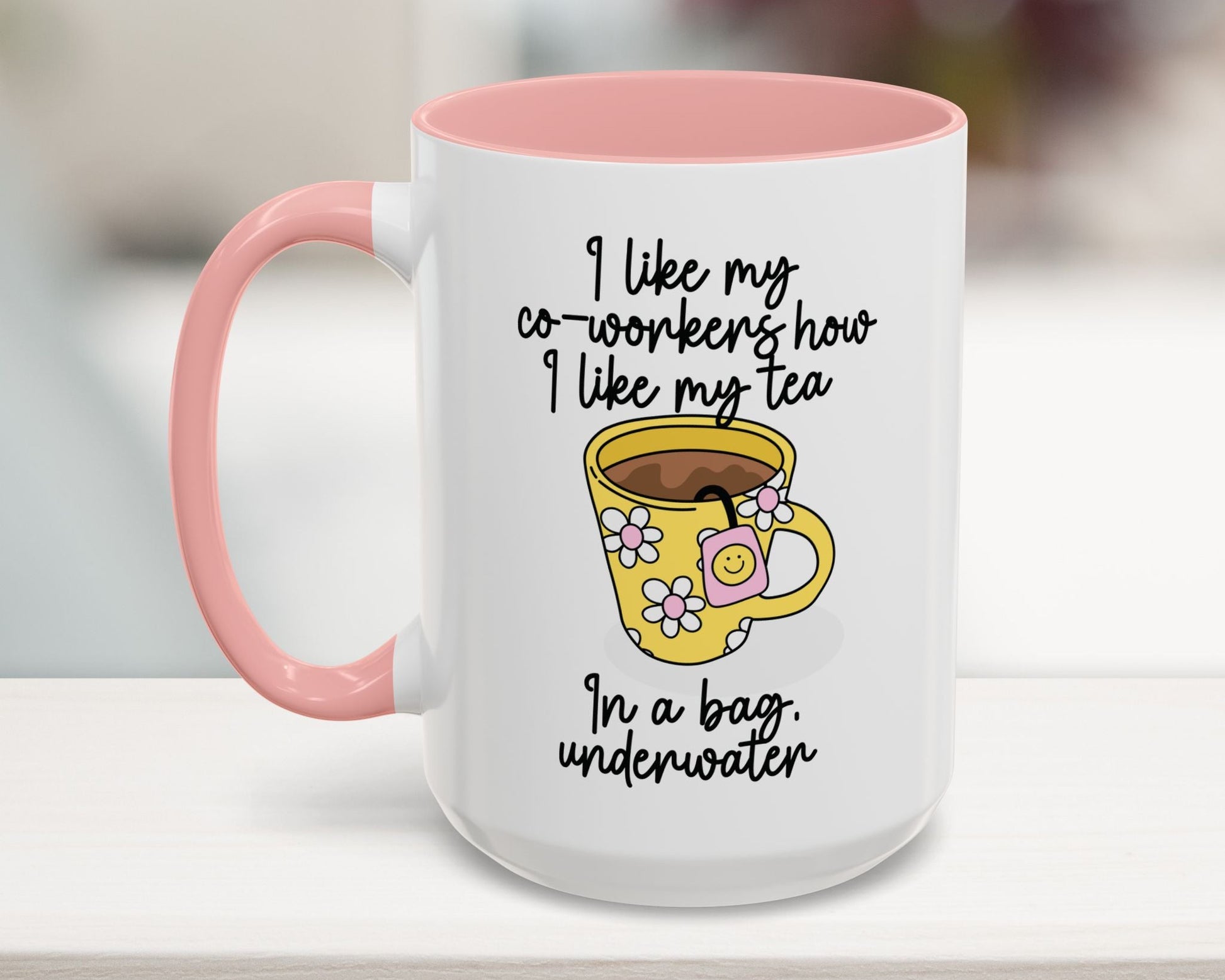 White mug with pink handle featuring a yellow coffee cup illustration and text on a blurred background
