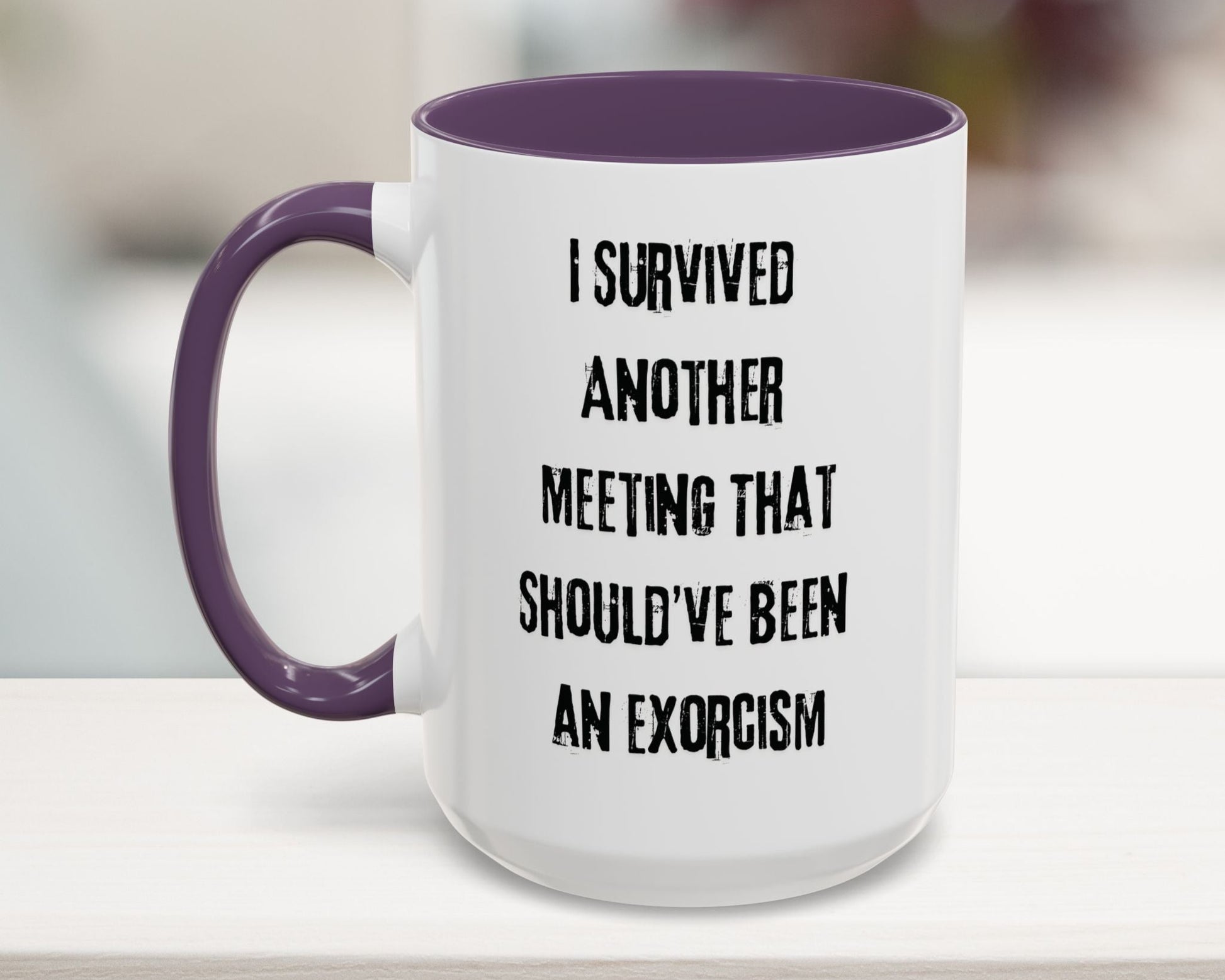 White mug with purple handle and text 'I survived another meeting that should've been an exorcism' on a blurred background