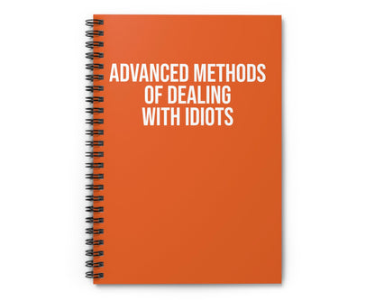 Orange notebook with 'Advanced Methods of Dealing with Idiots' text on a white background