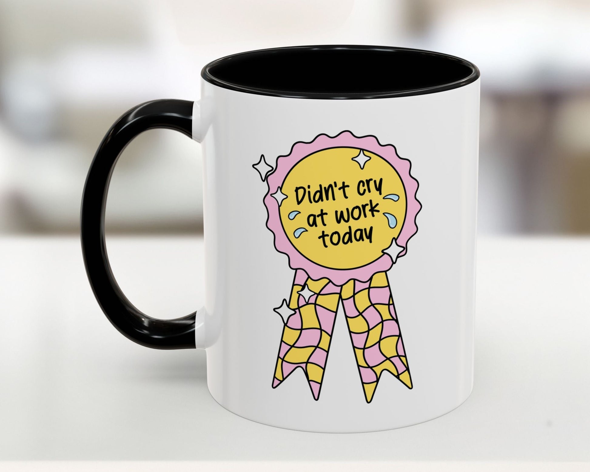 White mug with black handle featuring a colorful design and text on a blurred background