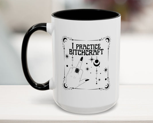 White mug with black interior and handle, featuring 'I Practice Bitchcraft' text and hand gesture design.