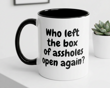Mug with text 'Who left the box of assholes open again?' on a white surface.
