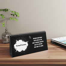 Desk calendar with motivational quote on a wooden surface with a plant in the background