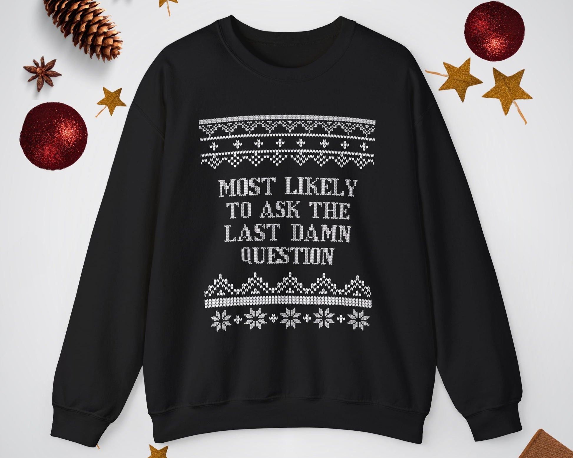 Black sweater with text 'Most likely to ask the last damn question' on a white background with Christmas decorations.