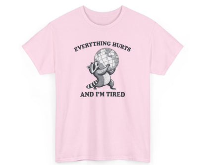 Light pink unisex tee featuring a tired raccoon with the phrase 'Everything Hurts and I’m Tired,' perfect for those who relate to the struggle.