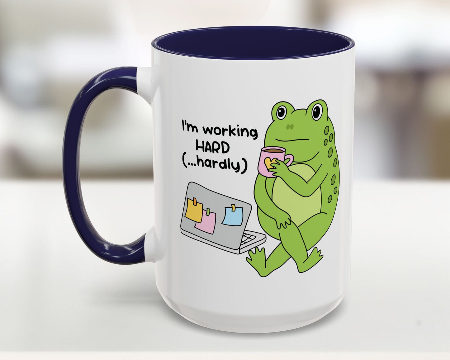 Mug with a green frog holding a cup and text 'I'm working HARD (...hardly)' on a white background