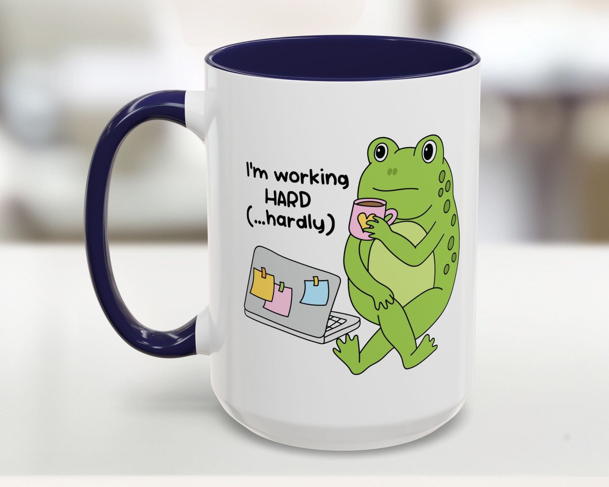 Mug with a green frog holding a cup and text 'I'm working HARD (...hardly)' on a white background