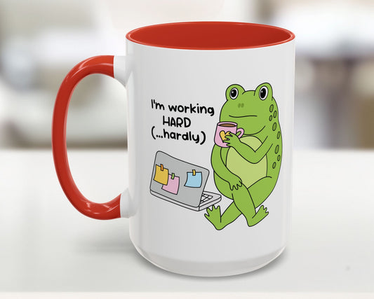 Mug with a green frog holding a cup and text 'I'm working HARD (...hardly)' on a white background