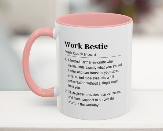 Mug with pink interior and handle featuring a definition of 'Work Bestie' on a blurred background
