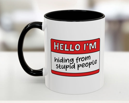 White mug with black interior and handle, featuring a red label with text on a blurred background.