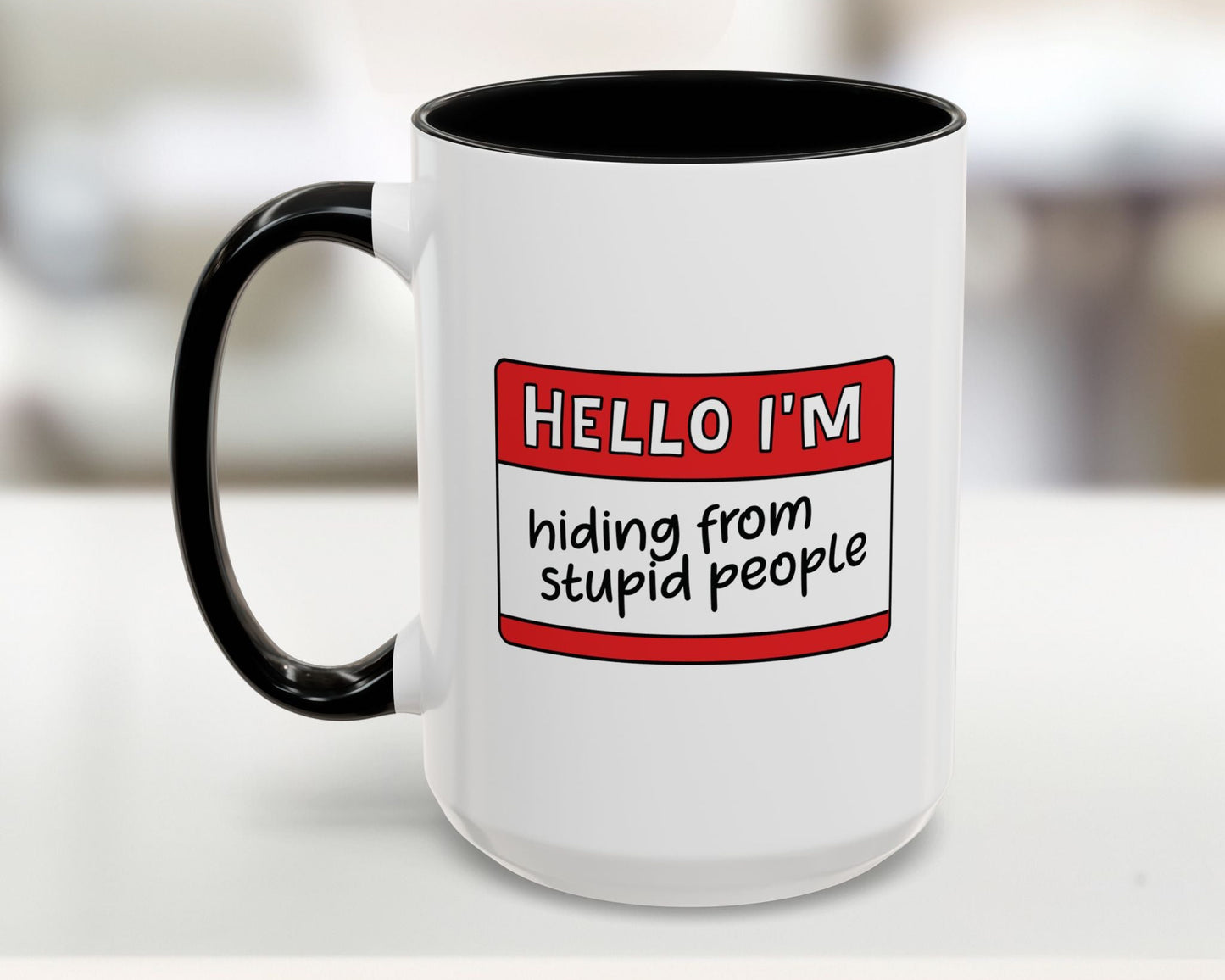 White mug with black interior and handle, featuring a red name tag with text on a blurred background.