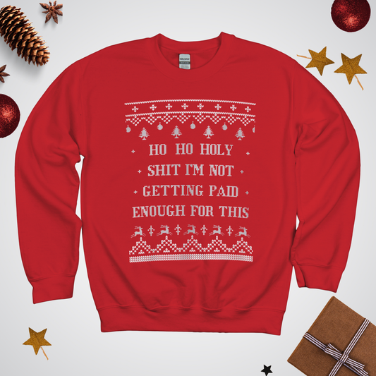Red sweater with white text and patterns on a light gray background with Christmas decorations.