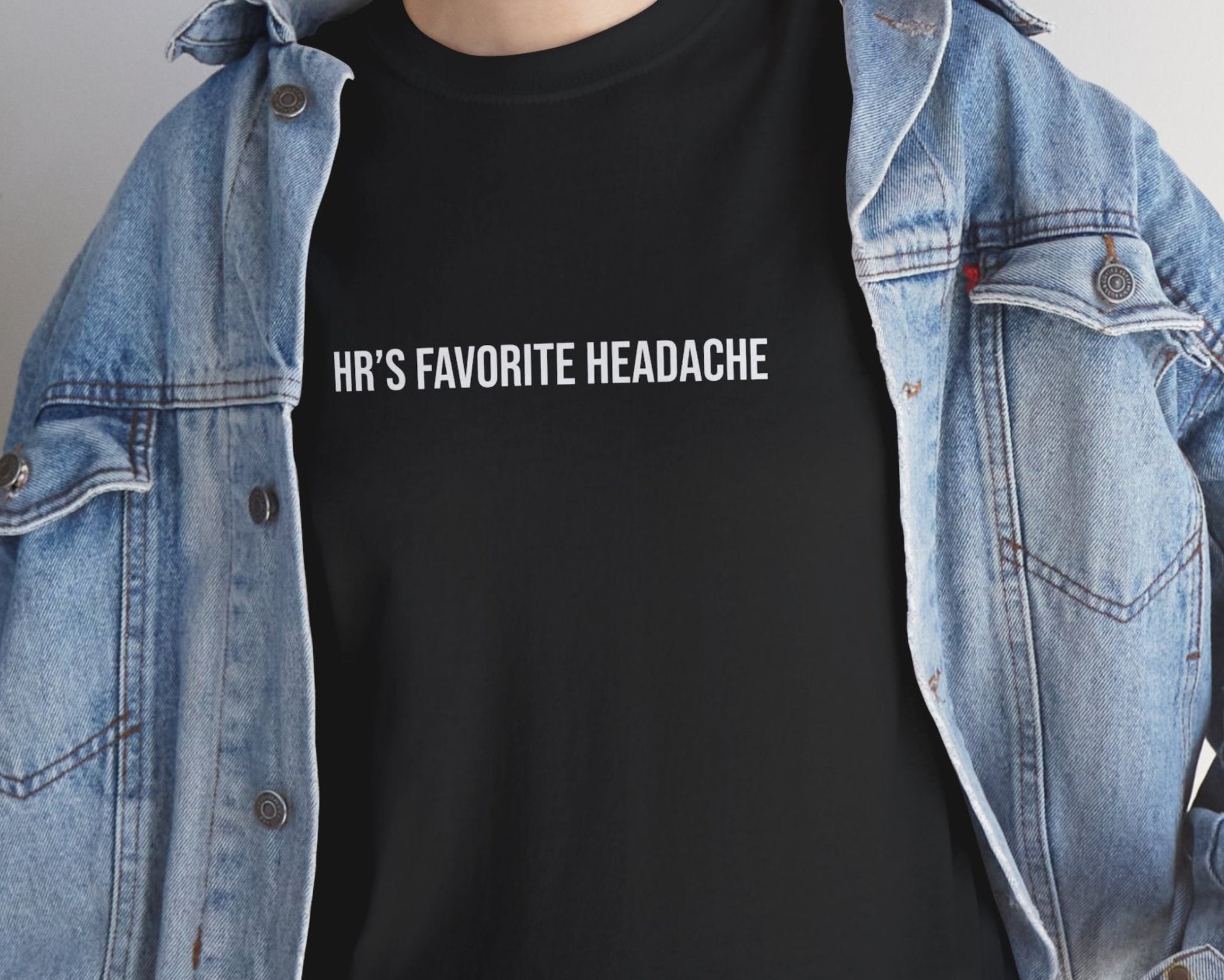 Person wearing a black t-shirt with text and a denim jacket indoors.