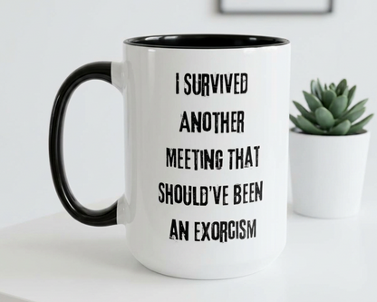Mug with text 'I survived another meeting that should've been an exorcism' on a white surface with a plant in the background.