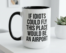 White mug with black interior and handle, featuring text on a white surface with a plant in the background.