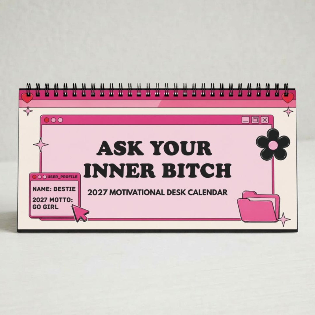 A pink and white spiral-bound desk calendar with black text reading 'ASK YOUR INNER BITCH 2027 MOTIVATIONAL DESK CALENDAR' and cartoon-style folder and flower graphics, photographed on a light neutral background.
