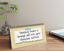 Notebook with a humorous skincare routine quote on a desk with a plant and magazine in the background.