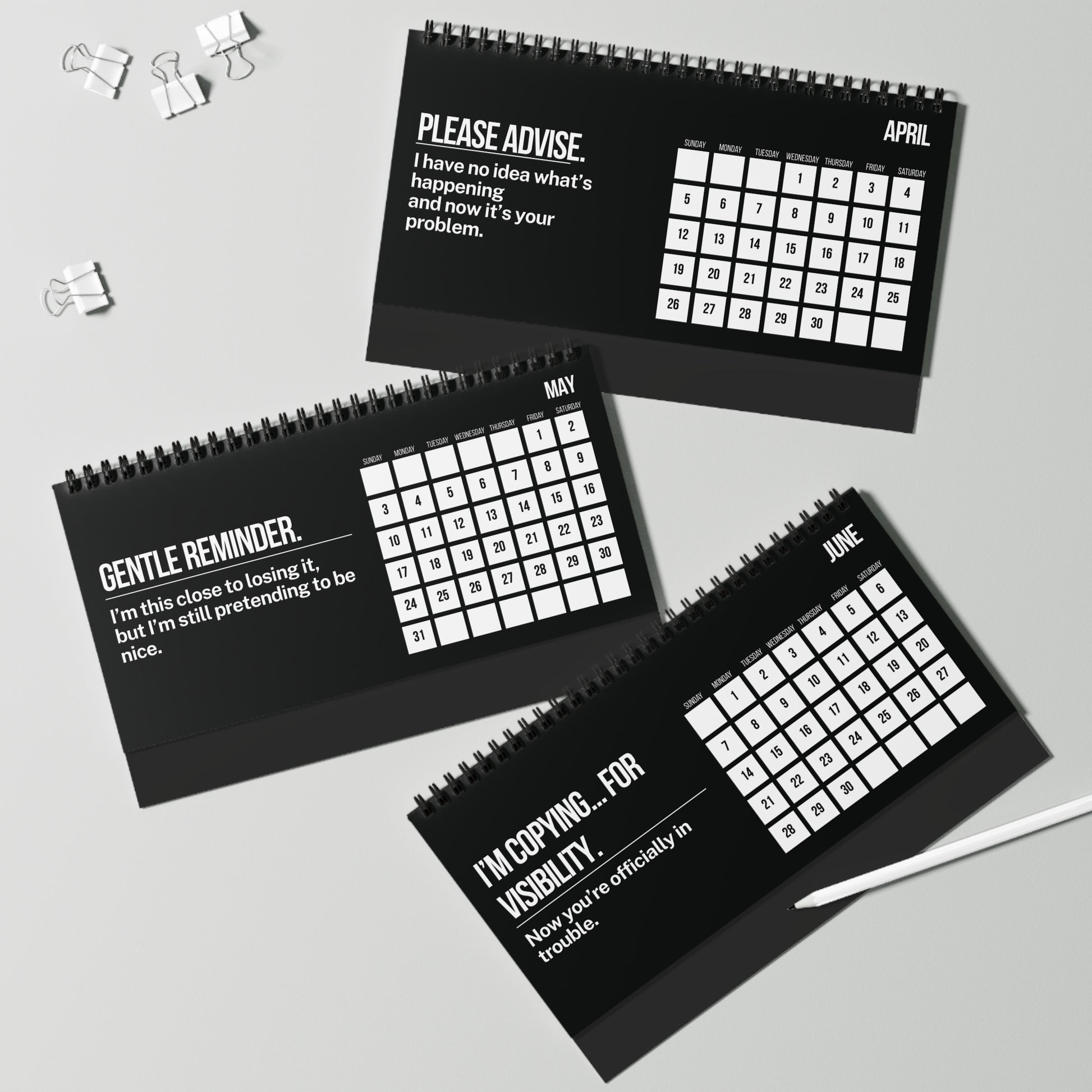 Three black spiral-bound calendars with humorous text for April, May, and June on a light gray background.