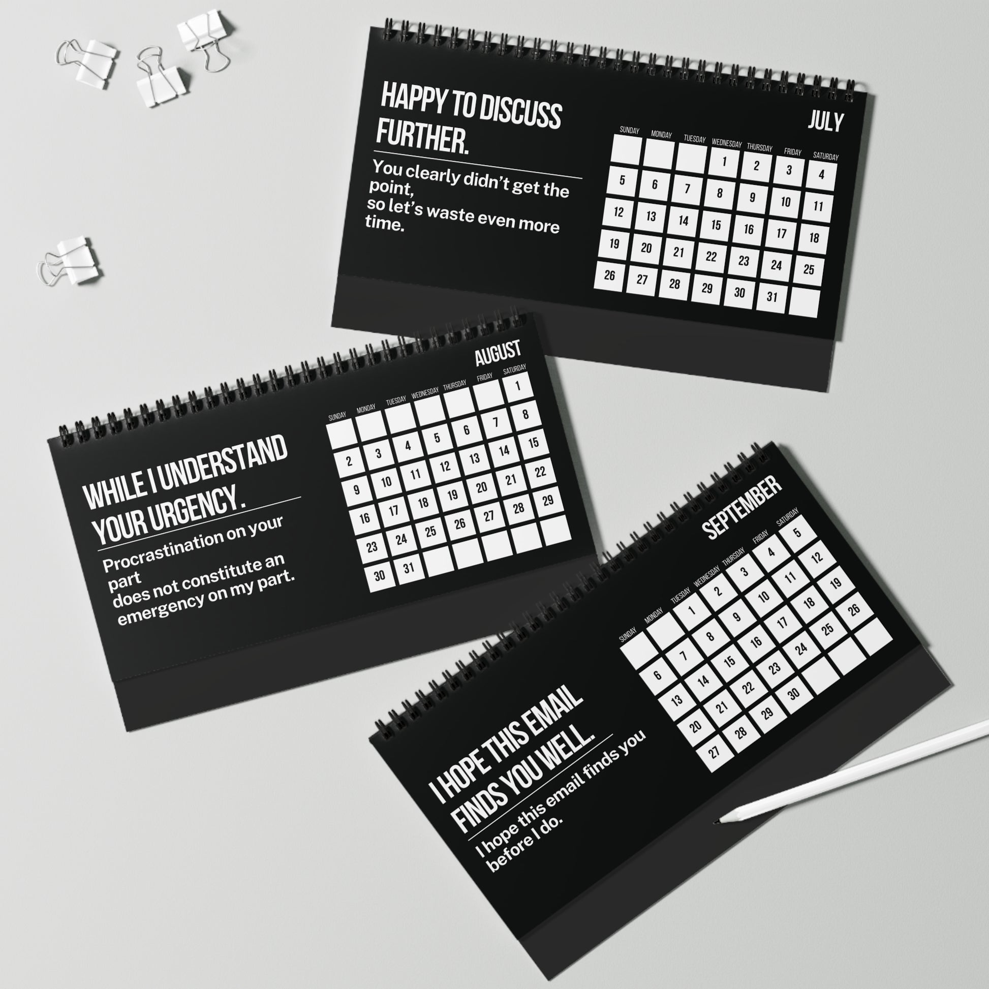 Three black spiral-bound calendars with white text on a gray surface.