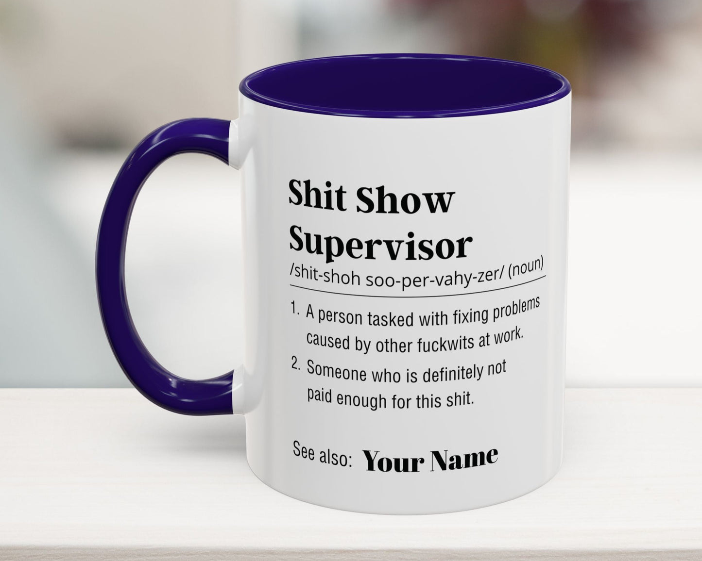 Mug with text definition of 'Shit Show Supervisor' on a blurred background