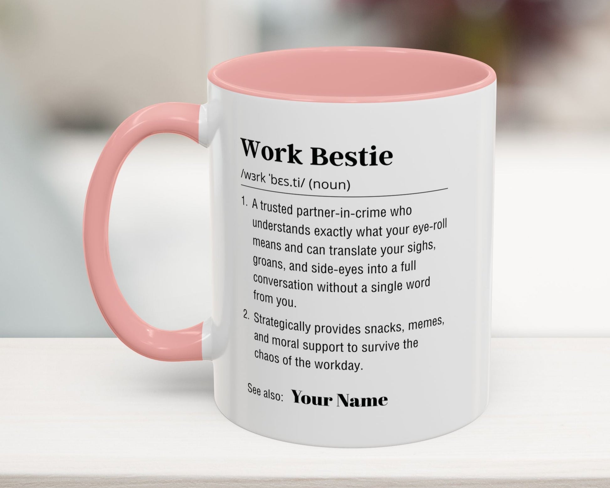 Mug with pink interior and handle, featuring a definition of 'Work Bestie' on a blurred background.