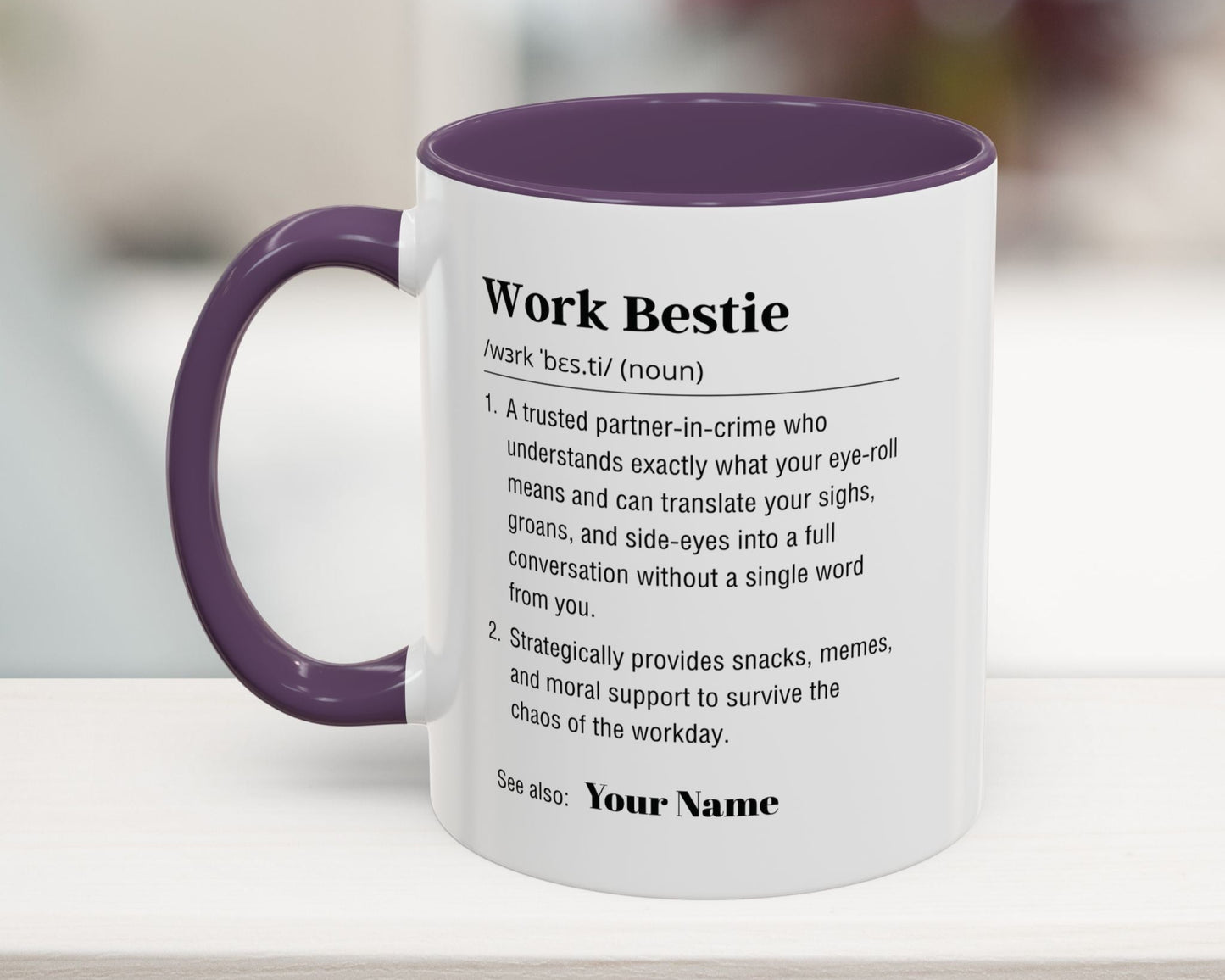 Mug with purple interior and handle, featuring text definition of 'Work Bestie' on a blurred background.