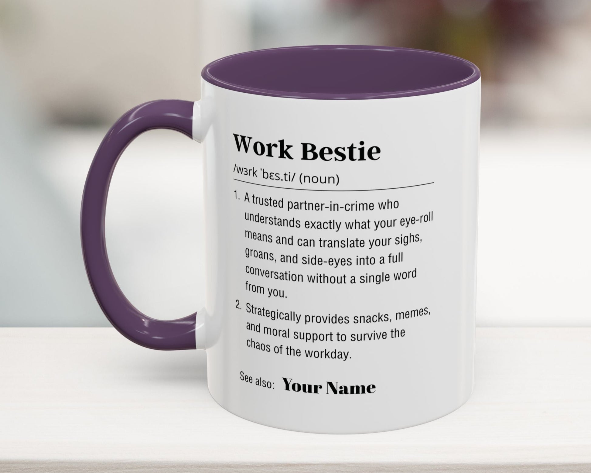 Mug with purple interior and handle, featuring text definition of 'Work Bestie' on a blurred background.