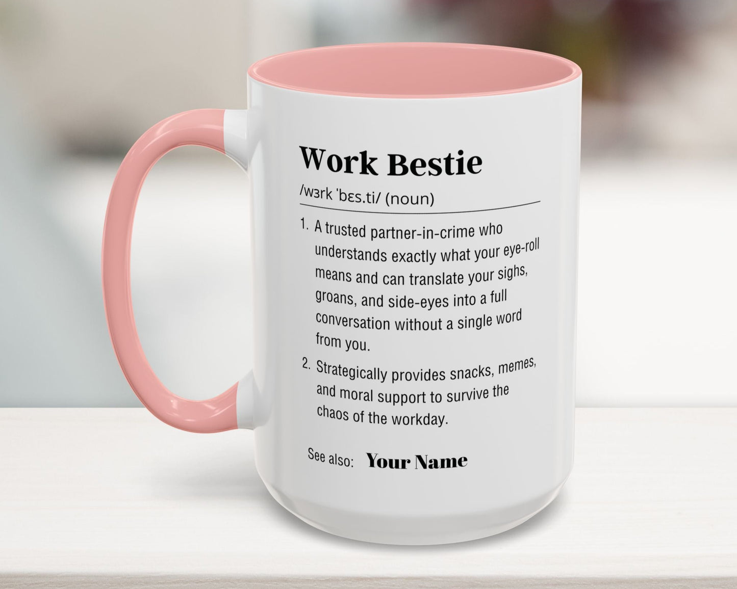 Mug with pink interior and handle on a wooden surface, featuring text about 'Work Bestie'.