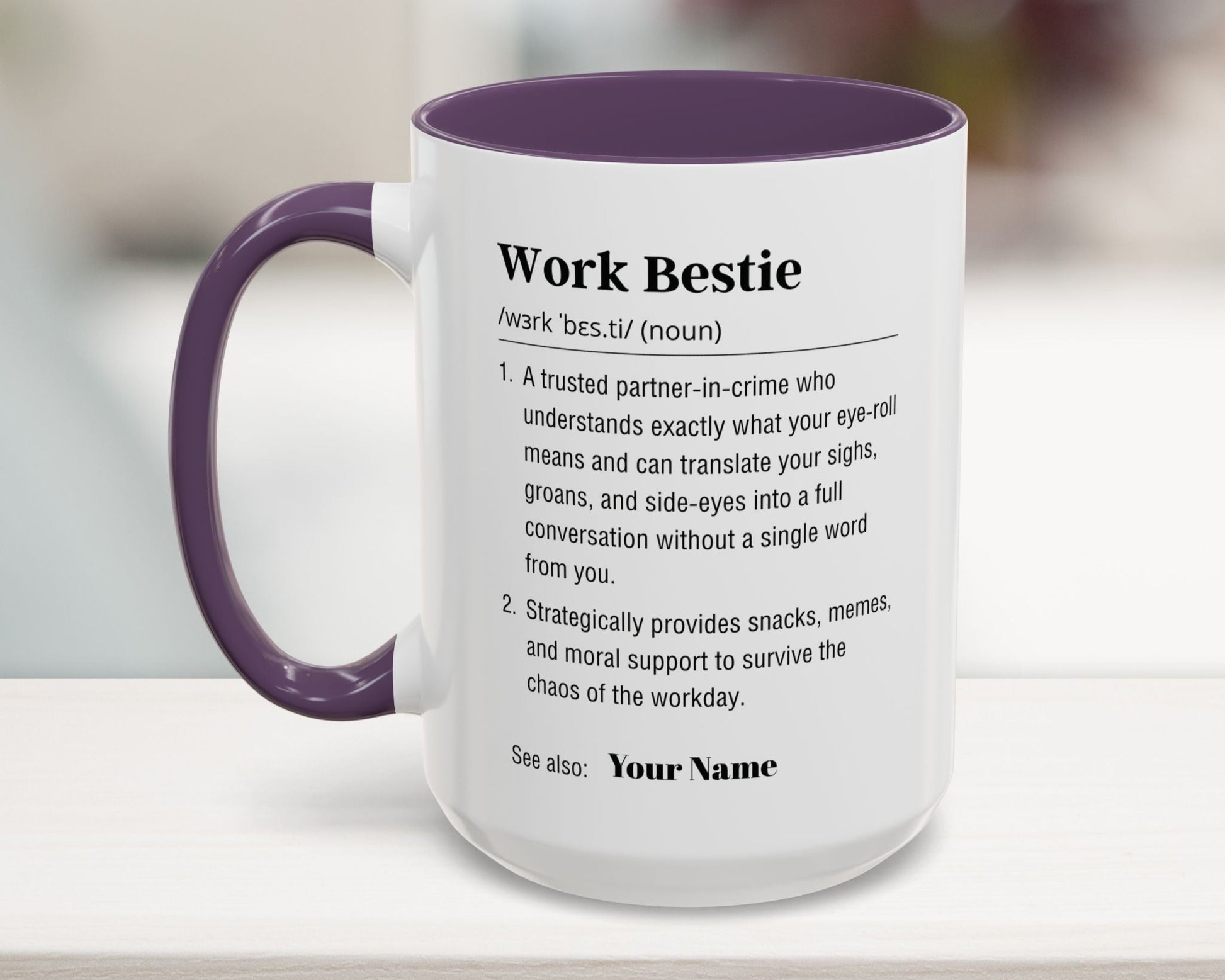 Mug with purple handle and interior, featuring a definition of 'Work Bestie' on a blurred background.