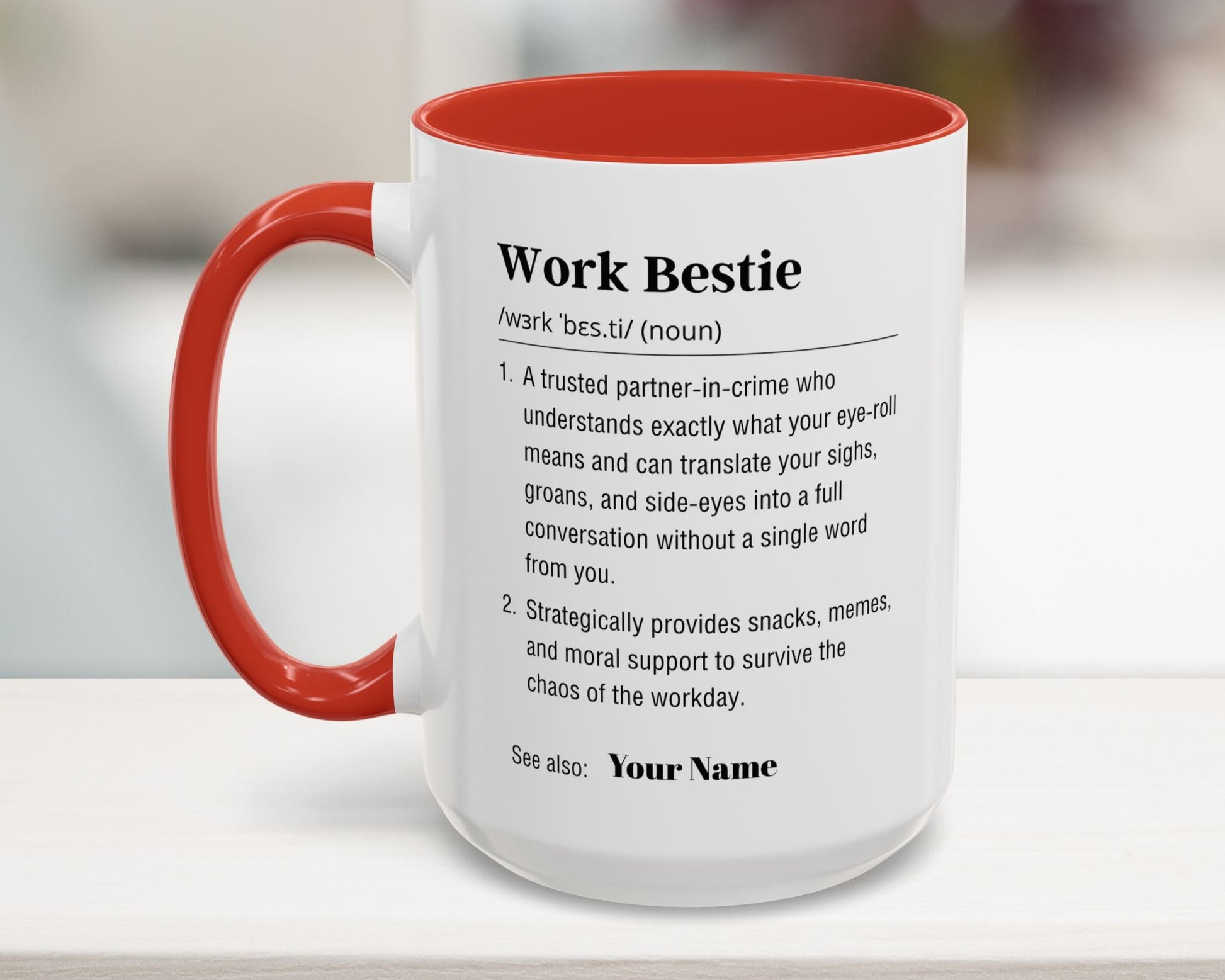 Mug with red interior and handle, featuring a definition of 'Work Bestie' on a blurred background.