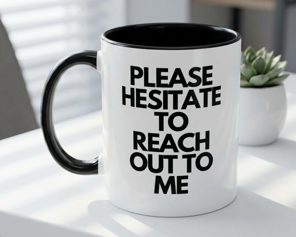 White mug with black interior and handle, featuring text on a white surface with a plant in the background.