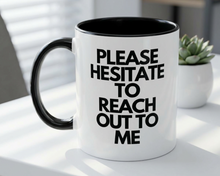 White mug with black interior and handle, featuring text on a white surface with a plant in the background.