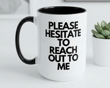 White mug with black interior and handle, featuring text 'PLEASE HESITATE TO REACH OUT TO ME' on a light gray surface.