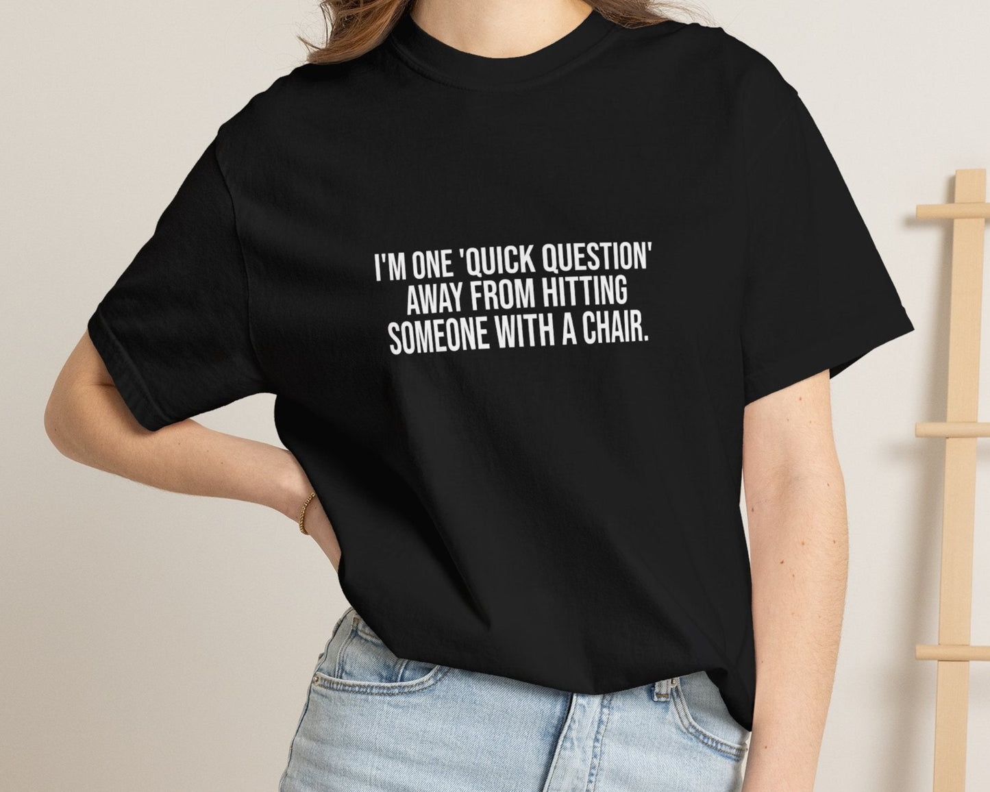 Person wearing a black t-shirt with text, standing against a neutral background