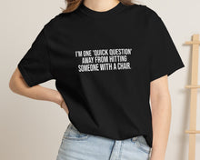 Person wearing a black t-shirt with text, standing against a neutral background